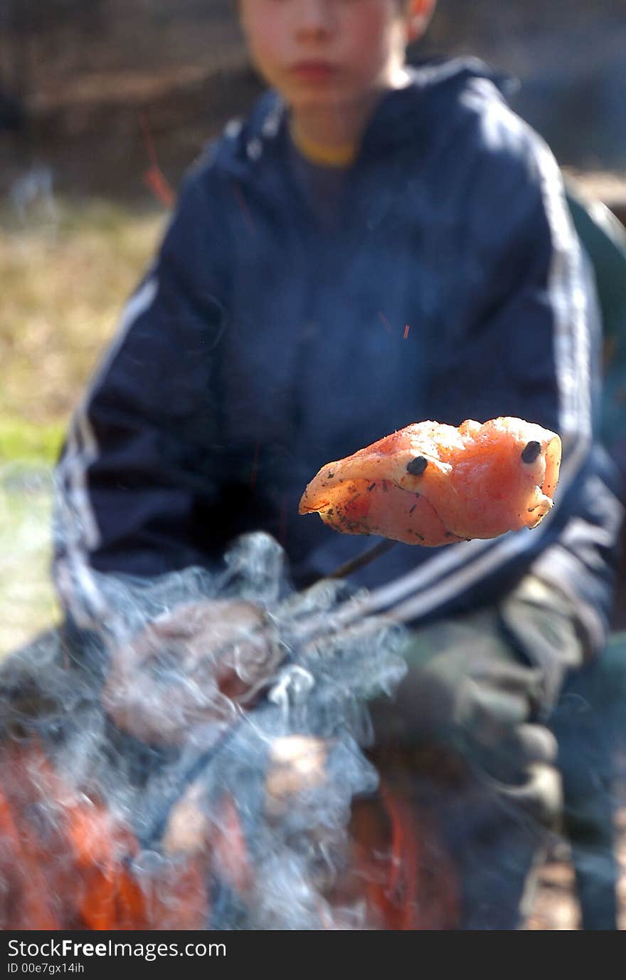 Young boy grill meat on fire outside