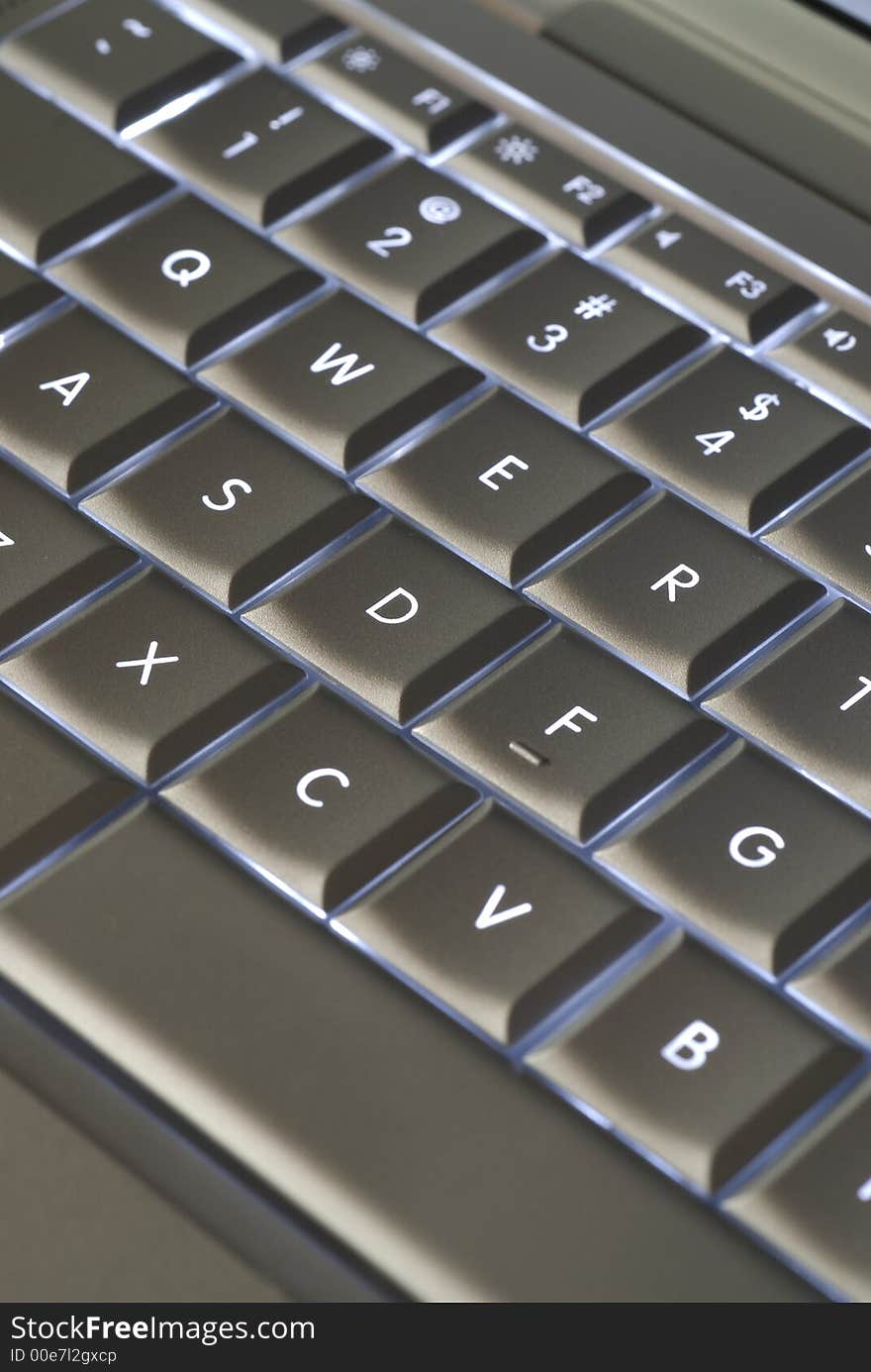 A closeup of a backlit computer keyboard with shallow depth of field and something of an optical illusion due to angle of image capture.