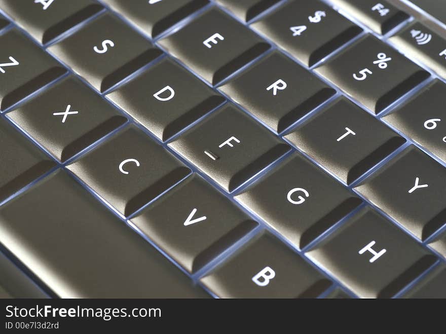 A closeup of a backlit computer keyboard with shallow depth of field and something of an optical illusion due to angle of image capture.