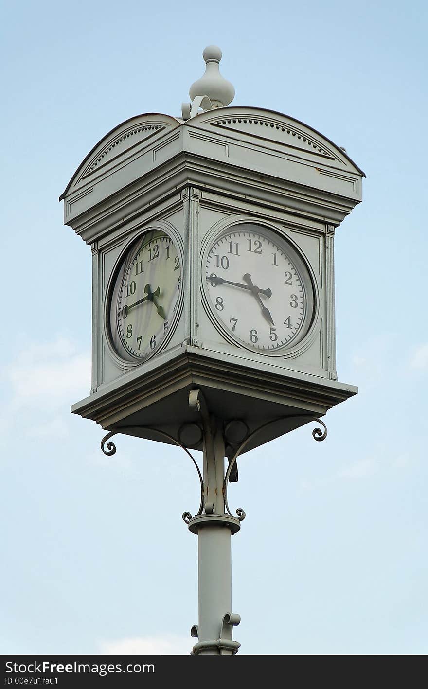 Street clock in Budapest at quarter to five against blue sky.