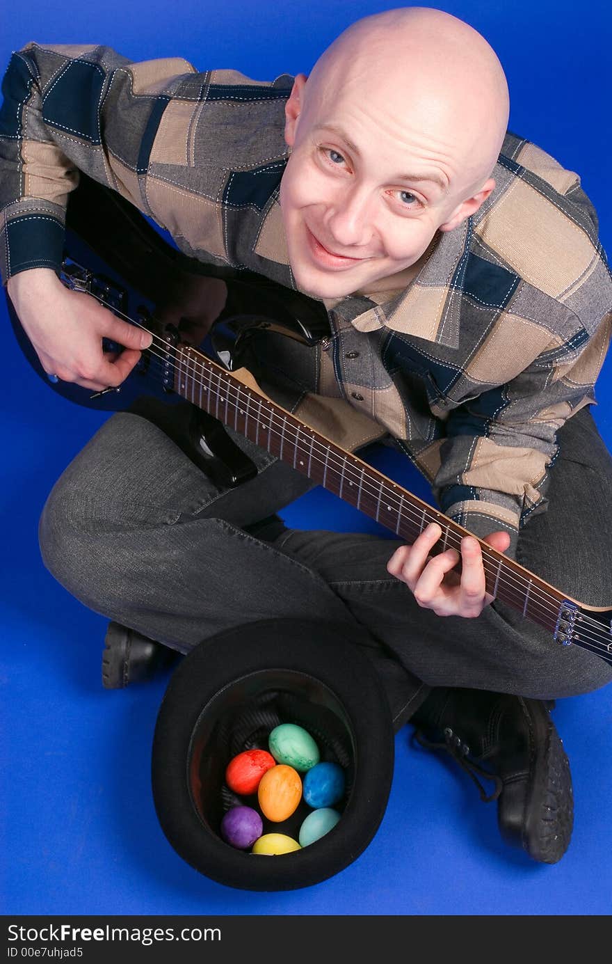 The musician with a guitar and easter eggs sits on a dark blue background. The musician with a guitar and easter eggs sits on a dark blue background