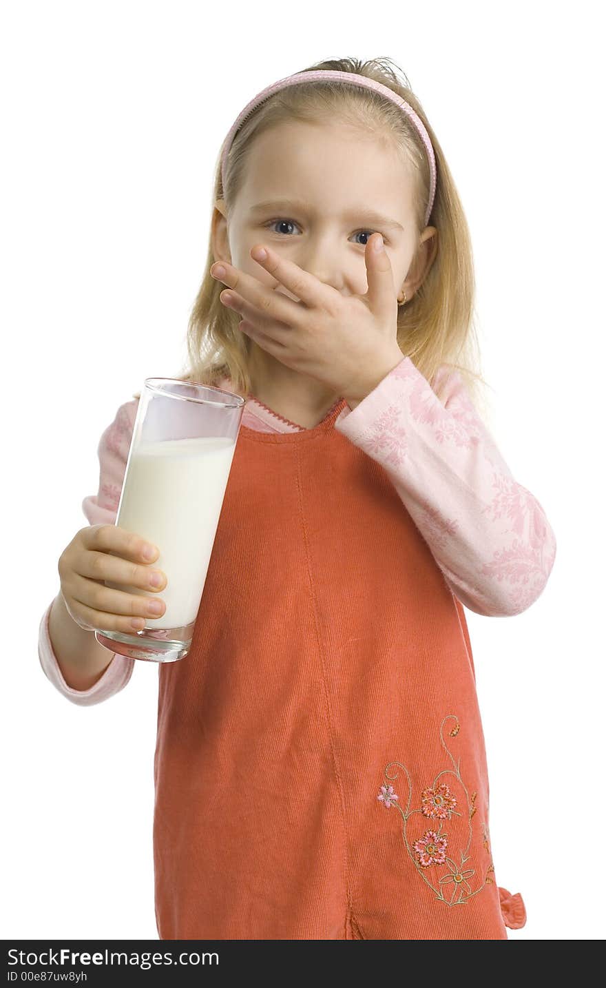 5-6yo girl standing with glass of milk and looking at camera. She's wiping off milky moustache by her hand. Isolated on white in studio.