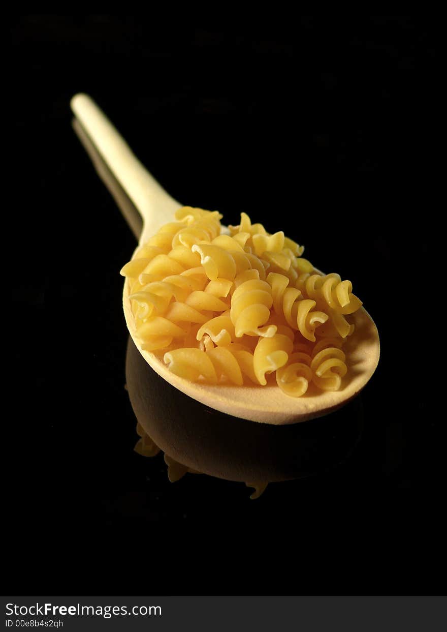 Uncooked pasta and tablespoon on black background