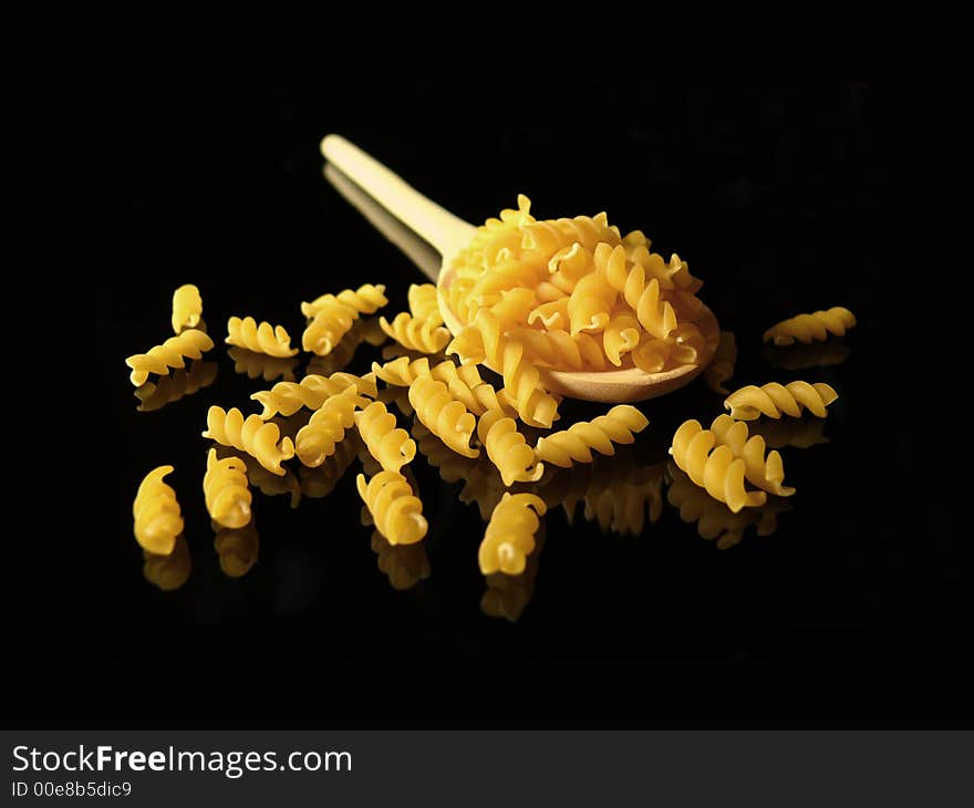 Uncooked pasta and tablespoon on black background