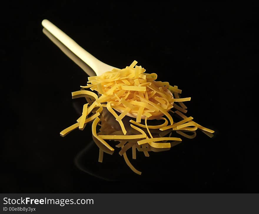 Uncooked pasta and tablespoon on black background