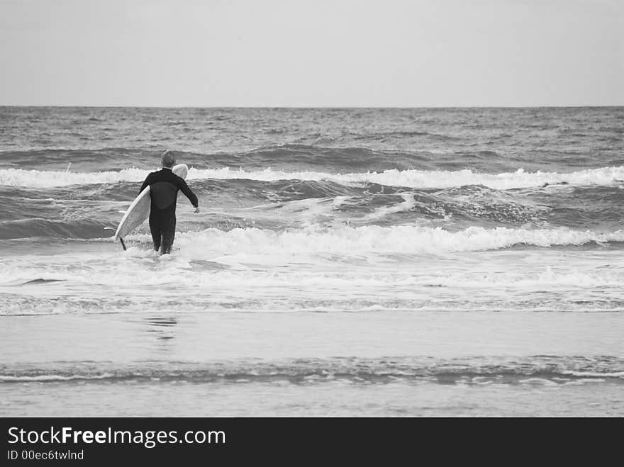 A lone surfer prepares to brave the breakers on an overcast windy day. A lone surfer prepares to brave the breakers on an overcast windy day