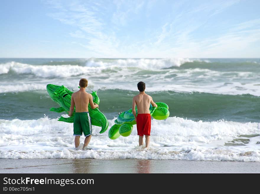 Two boys contemplate a tackling some serious surf with two pool toys. Two boys contemplate a tackling some serious surf with two pool toys