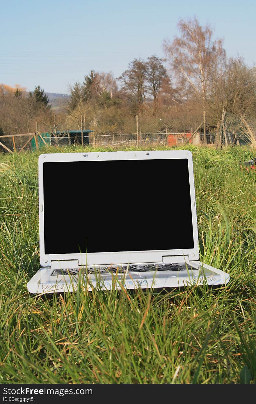 A wireless computer is on green grass with on a light blue sky. A wireless computer is on green grass with on a light blue sky