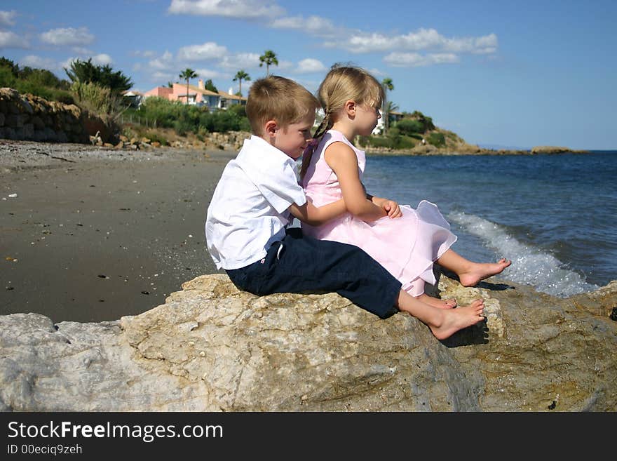 Two young children sat on a rock looking out to sea. Two young children sat on a rock looking out to sea