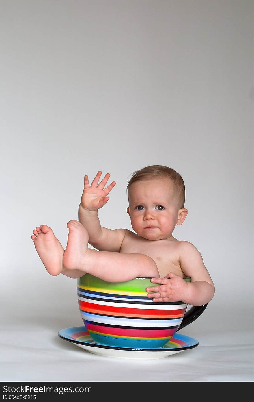 Image of an adorable baby sitting in a colorful, over-sized teacup. Image of an adorable baby sitting in a colorful, over-sized teacup