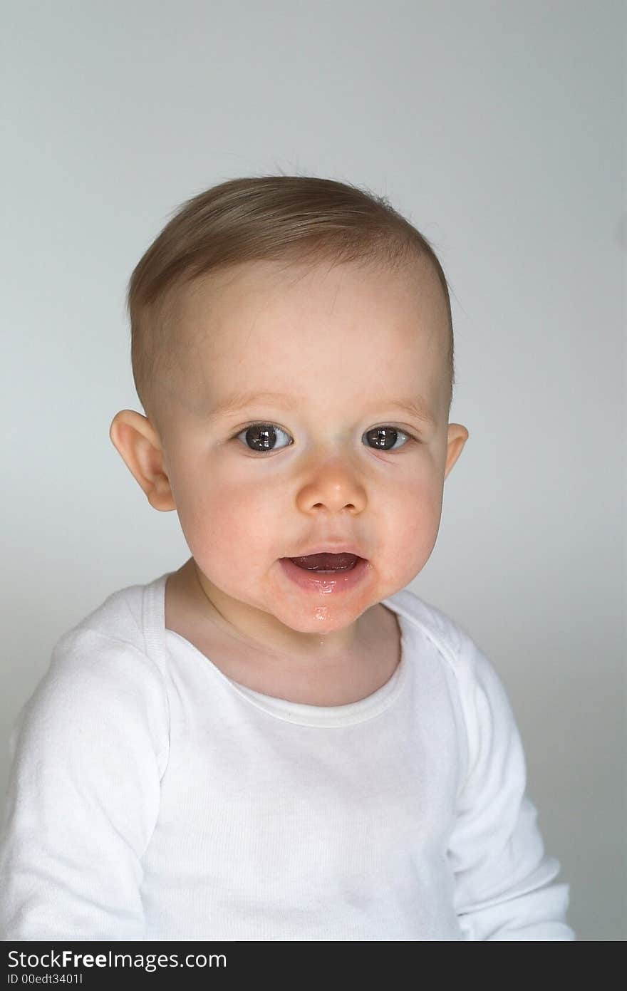 Image of a happy, smiling beautiful baby wearing a white shirt, sitting in front of a white background. Image of a happy, smiling beautiful baby wearing a white shirt, sitting in front of a white background