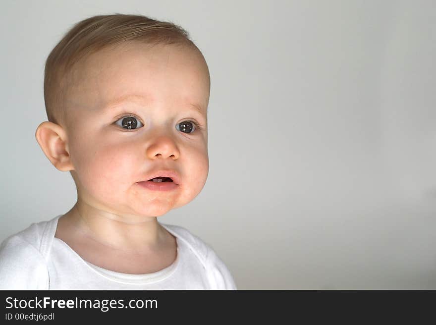 Image of a happy, smiling beautiful baby wearing a white shirt, sitting in front of a white background. Image of a happy, smiling beautiful baby wearing a white shirt, sitting in front of a white background