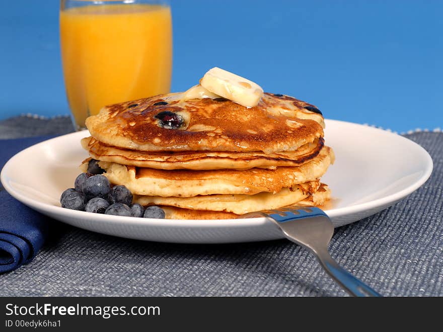 A stack of blueberry pancakes with maple syrup and orange juice. A stack of blueberry pancakes with maple syrup and orange juice