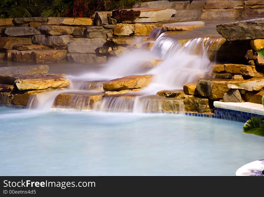 Long exposure of water falls entering a rocky vacation resort pool at night. Long exposure of water falls entering a rocky vacation resort pool at night