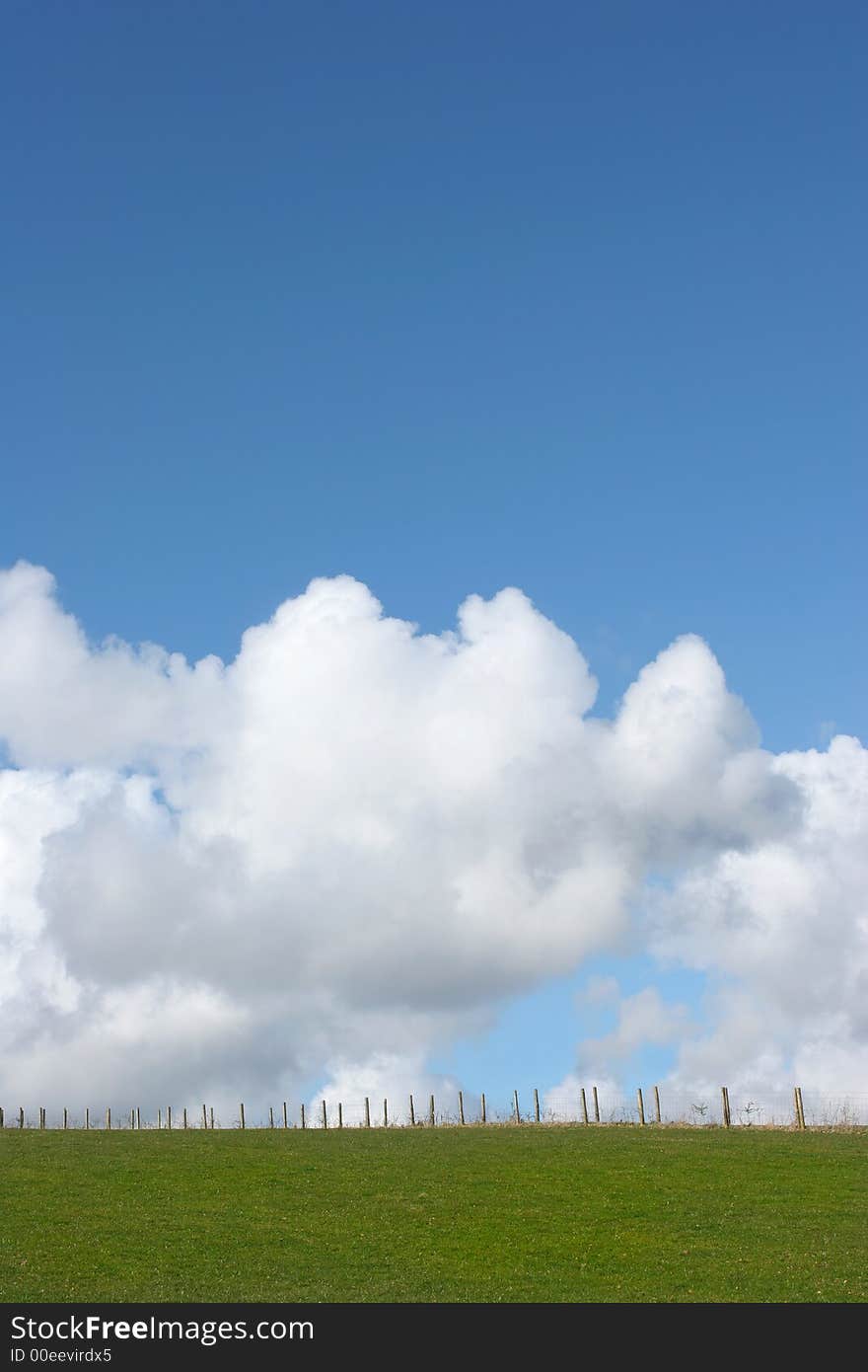 Wooden and wire fence in a field in rural countryside against a blue sky with cumulus clouds. Wooden and wire fence in a field in rural countryside against a blue sky with cumulus clouds.