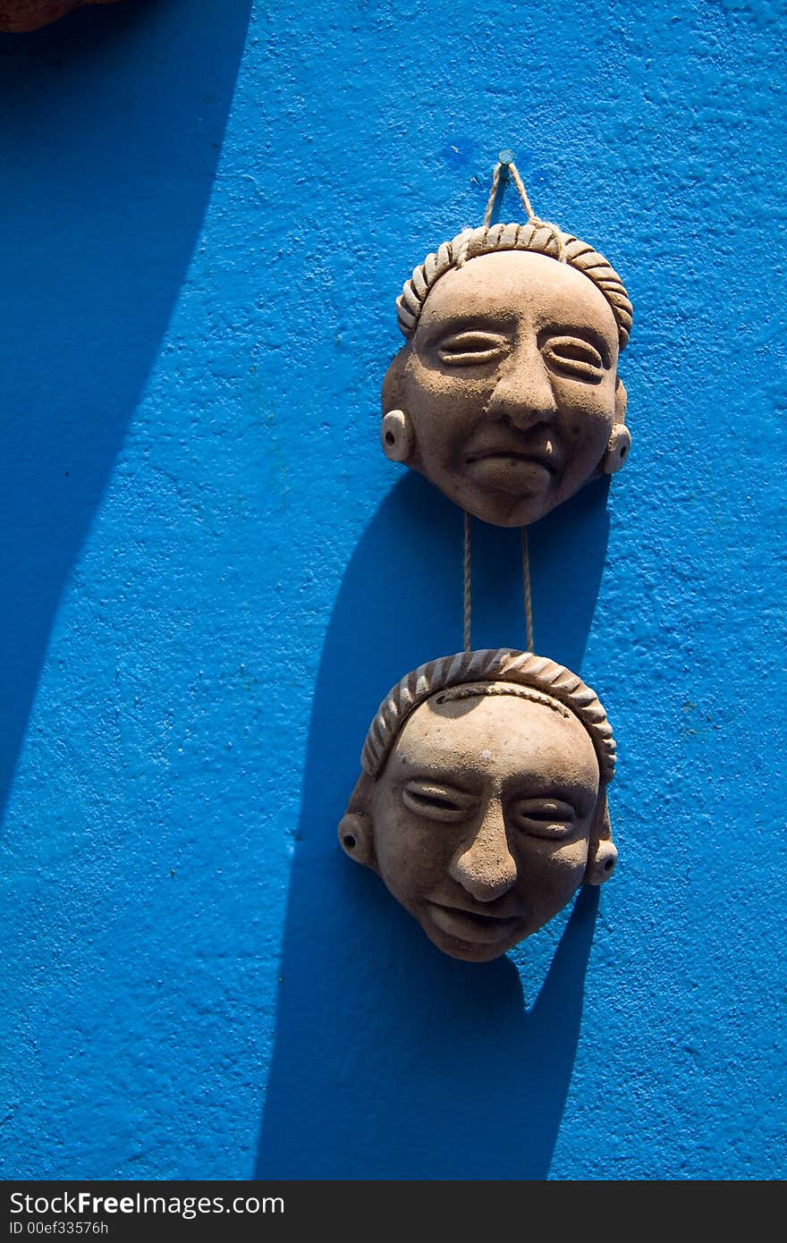 Two small ceramic masks hanging on a bright blue wall. Two small ceramic masks hanging on a bright blue wall