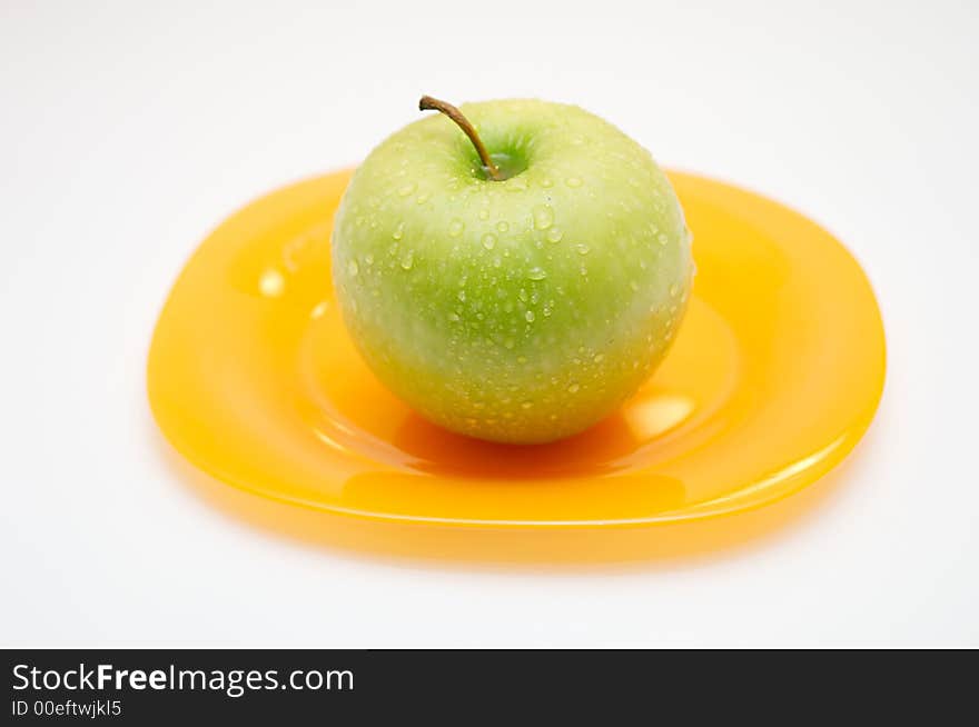 Green apple with drops of water on a yellow plate