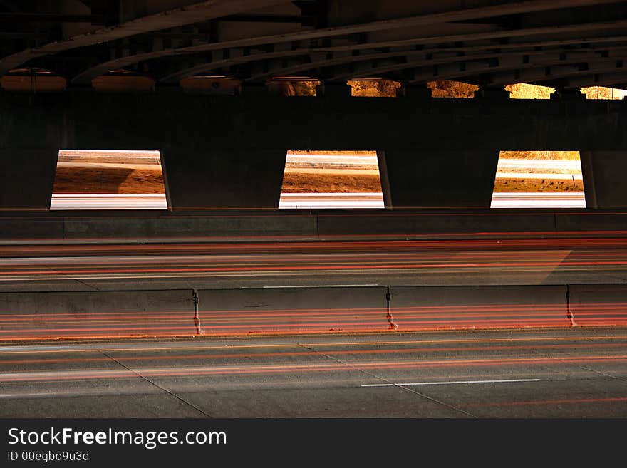 A scene from under bridge of highway where cars and trucks zoom past. A scene from under bridge of highway where cars and trucks zoom past