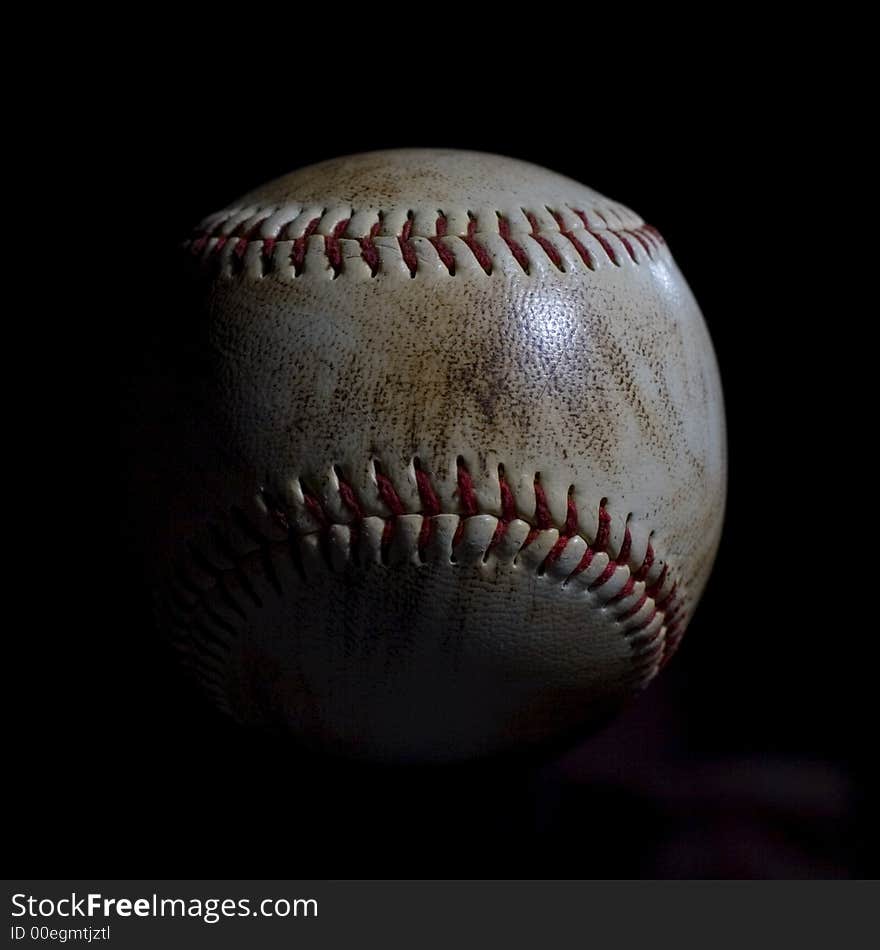 Dirty used baseball with red stitching isolated on black background