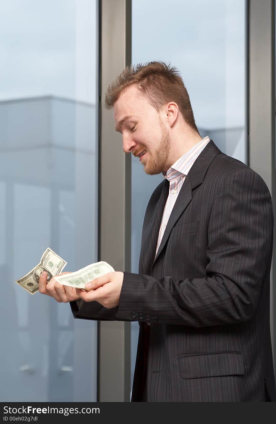 Sad businessman with money in hands on a background of a window. Sad businessman with money in hands on a background of a window