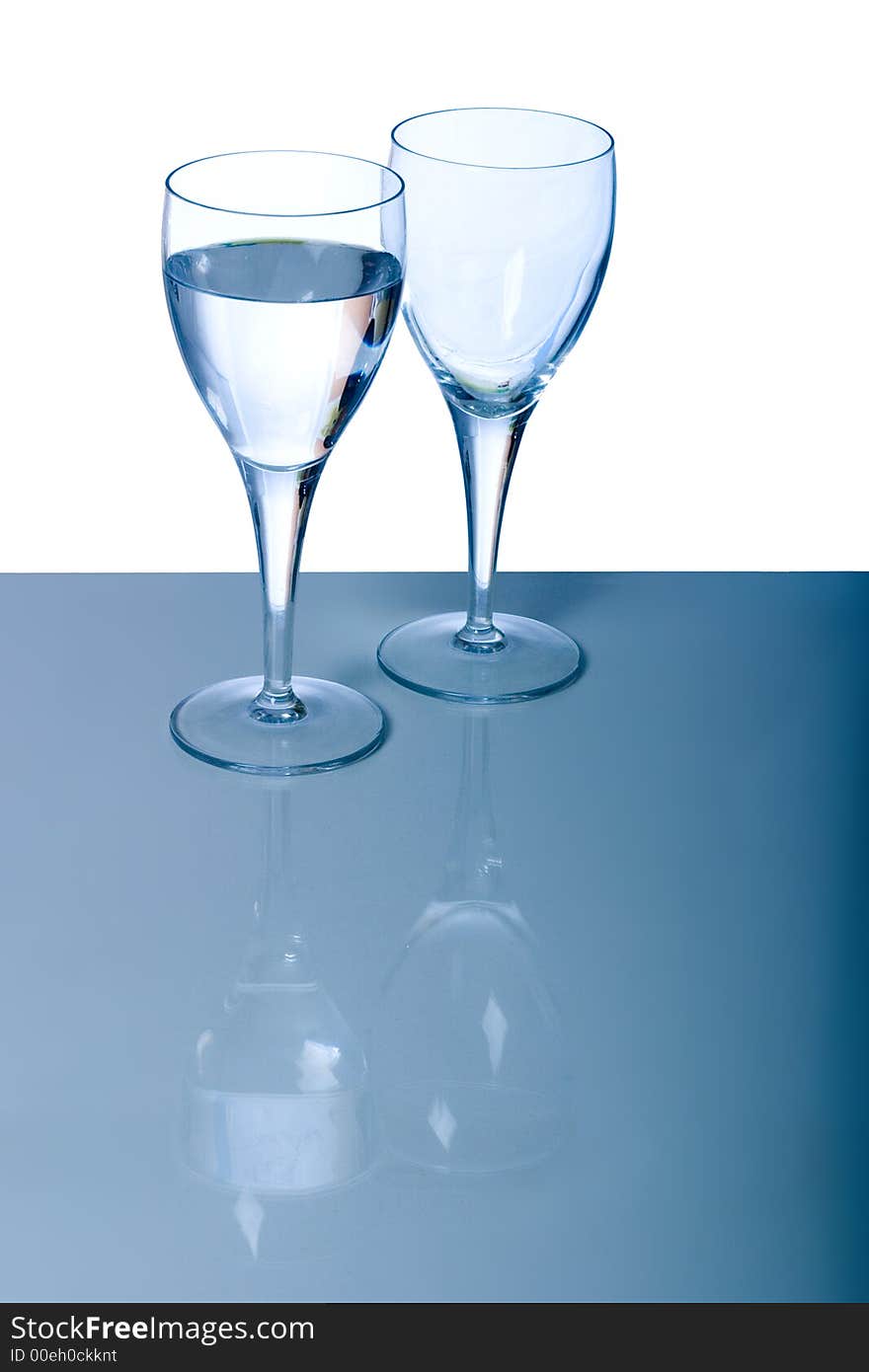 Full and empty glass against a white and blue background, reflected on the surface