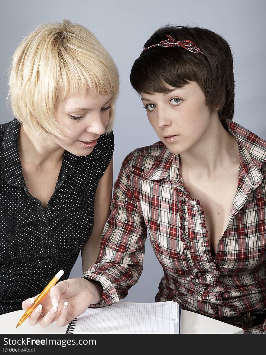 Two studying girls, blond and brunette, in a classroom. Two studying girls, blond and brunette, in a classroom