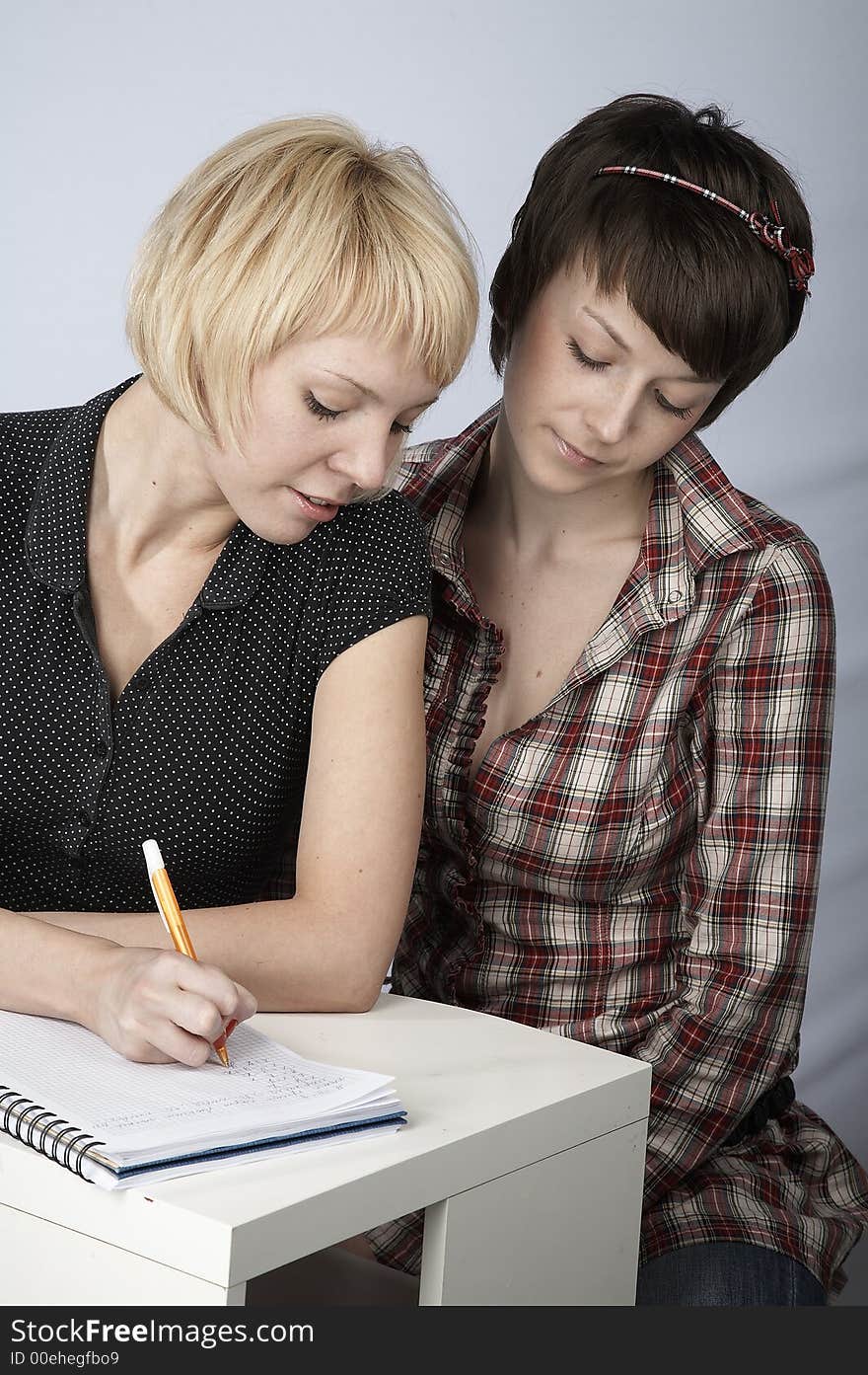 Two studying girls, blond and brunette, in a classroom. Two studying girls, blond and brunette, in a classroom