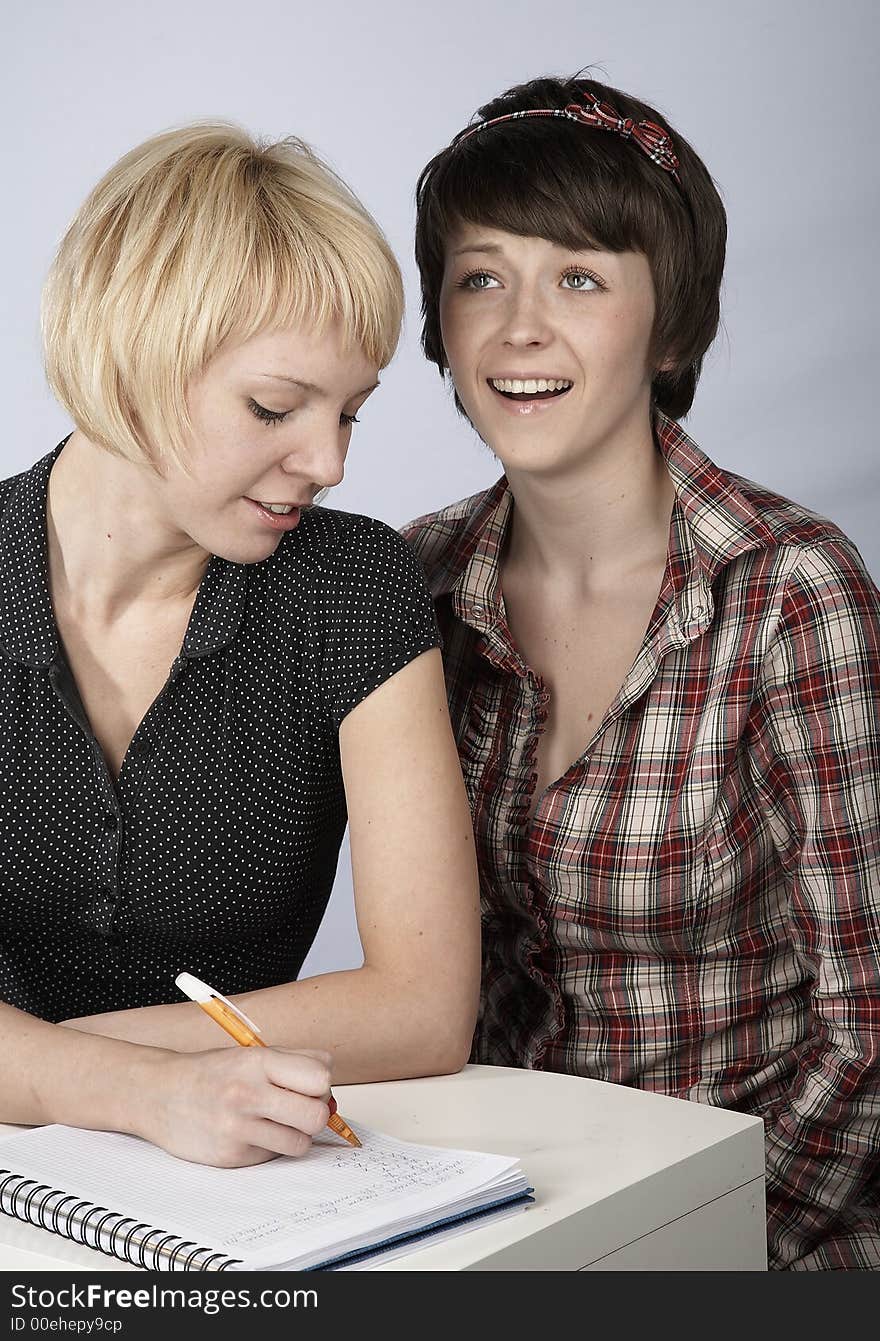 Two studying girls, blond and brunette, in a classroom. Two studying girls, blond and brunette, in a classroom