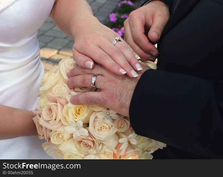 Detail of bride and groom's hands laid over bouquet of roses displaying wedding ring set. Detail of bride and groom's hands laid over bouquet of roses displaying wedding ring set