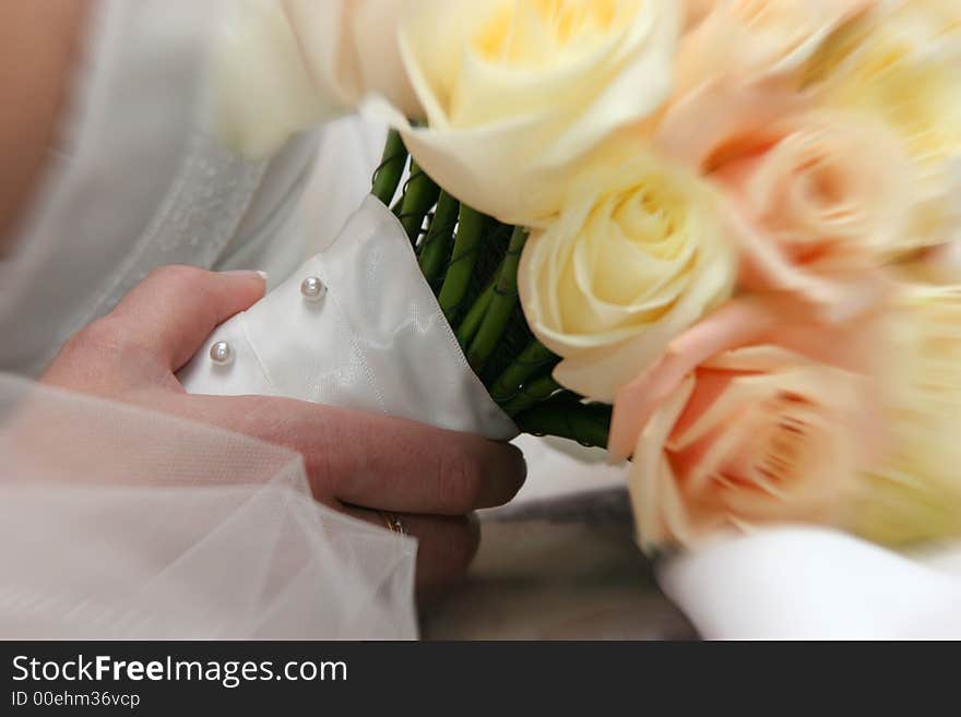 Detail of bride's hand holding bouquet of roses with satin and pearl wrap blur applied to edges for effect. Detail of bride's hand holding bouquet of roses with satin and pearl wrap blur applied to edges for effect