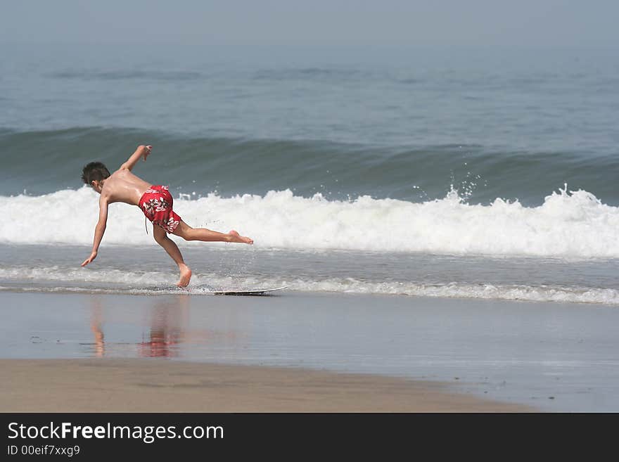 Boy making skimming and falling at the coastline