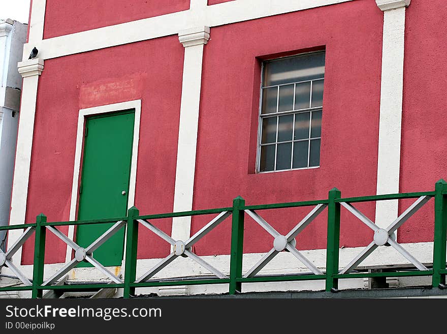 A bright pink stucco apartment or condo with a green door. A bright pink stucco apartment or condo with a green door