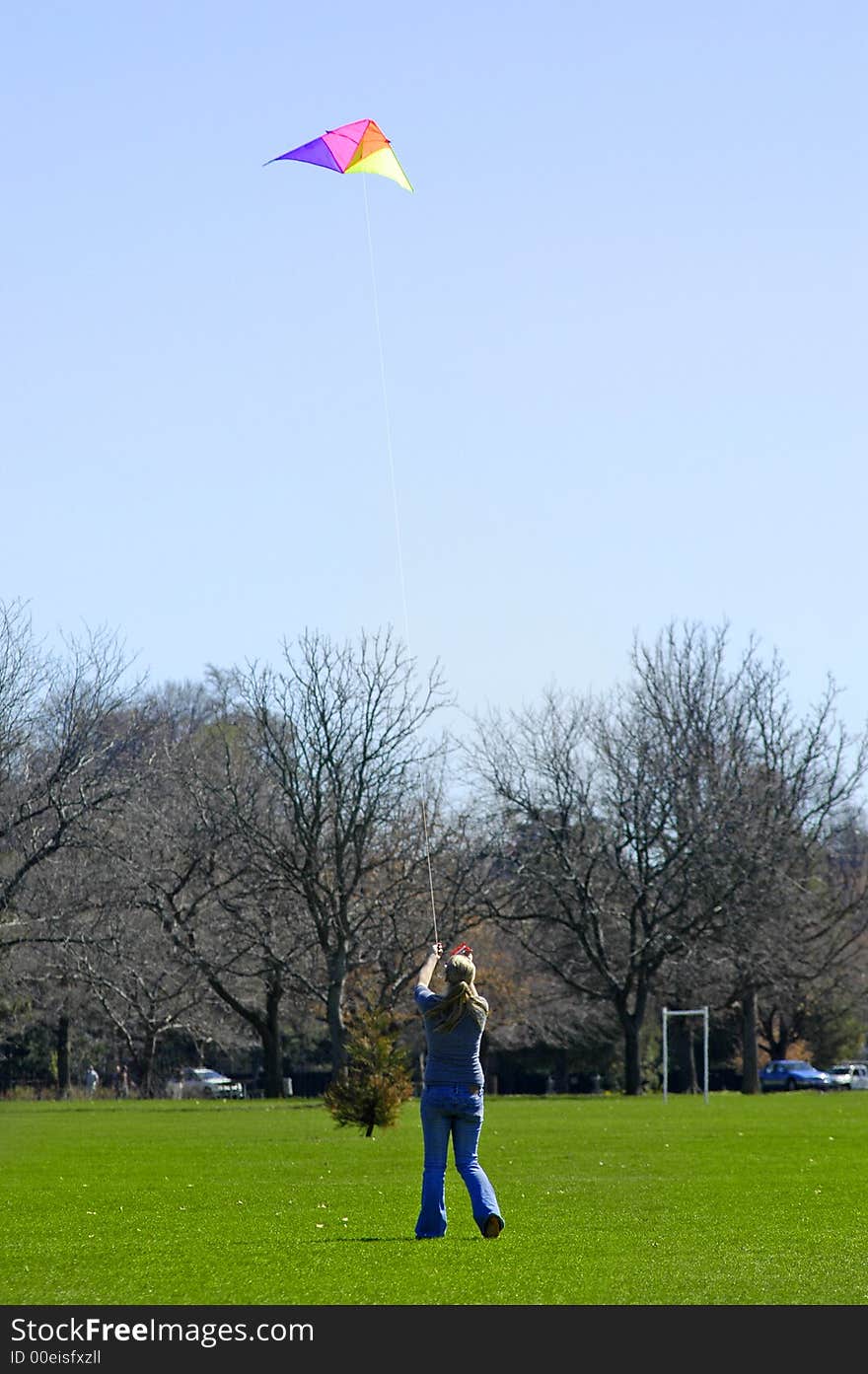 Girl flying a kite in a park with blue sky