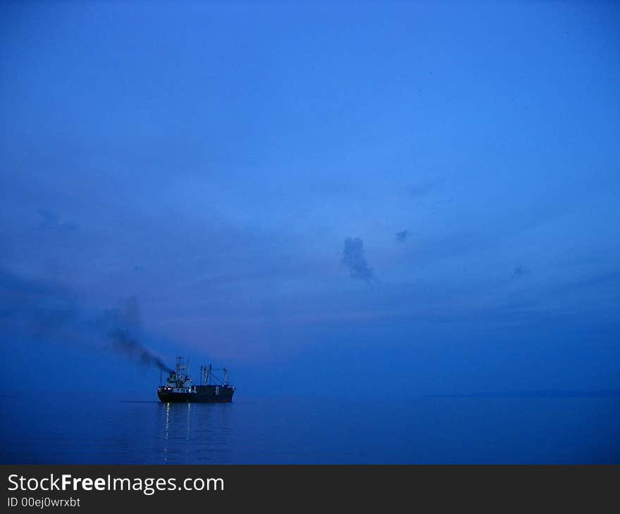 Freighter cargo ship sailing away from pier on a blue twilight. Freighter cargo ship sailing away from pier on a blue twilight