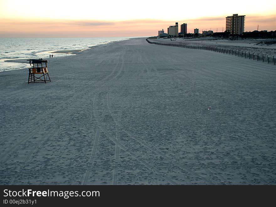 Dusk or sunset on a long stretch of sandy beach and water with pink sky at Pensacola Beach. Dusk or sunset on a long stretch of sandy beach and water with pink sky at Pensacola Beach.