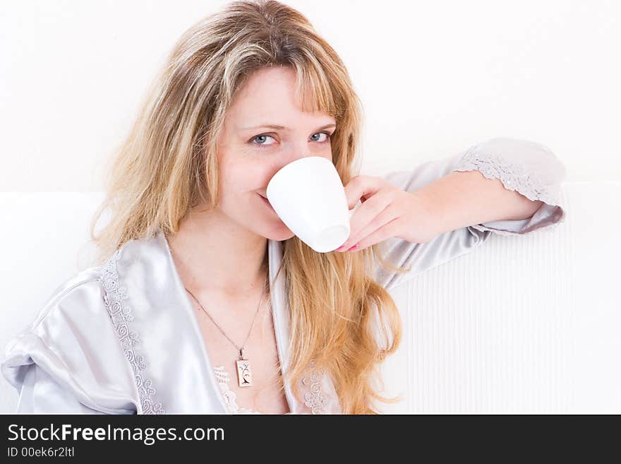 A women in a silver robe smiling whilst drinking a coffee