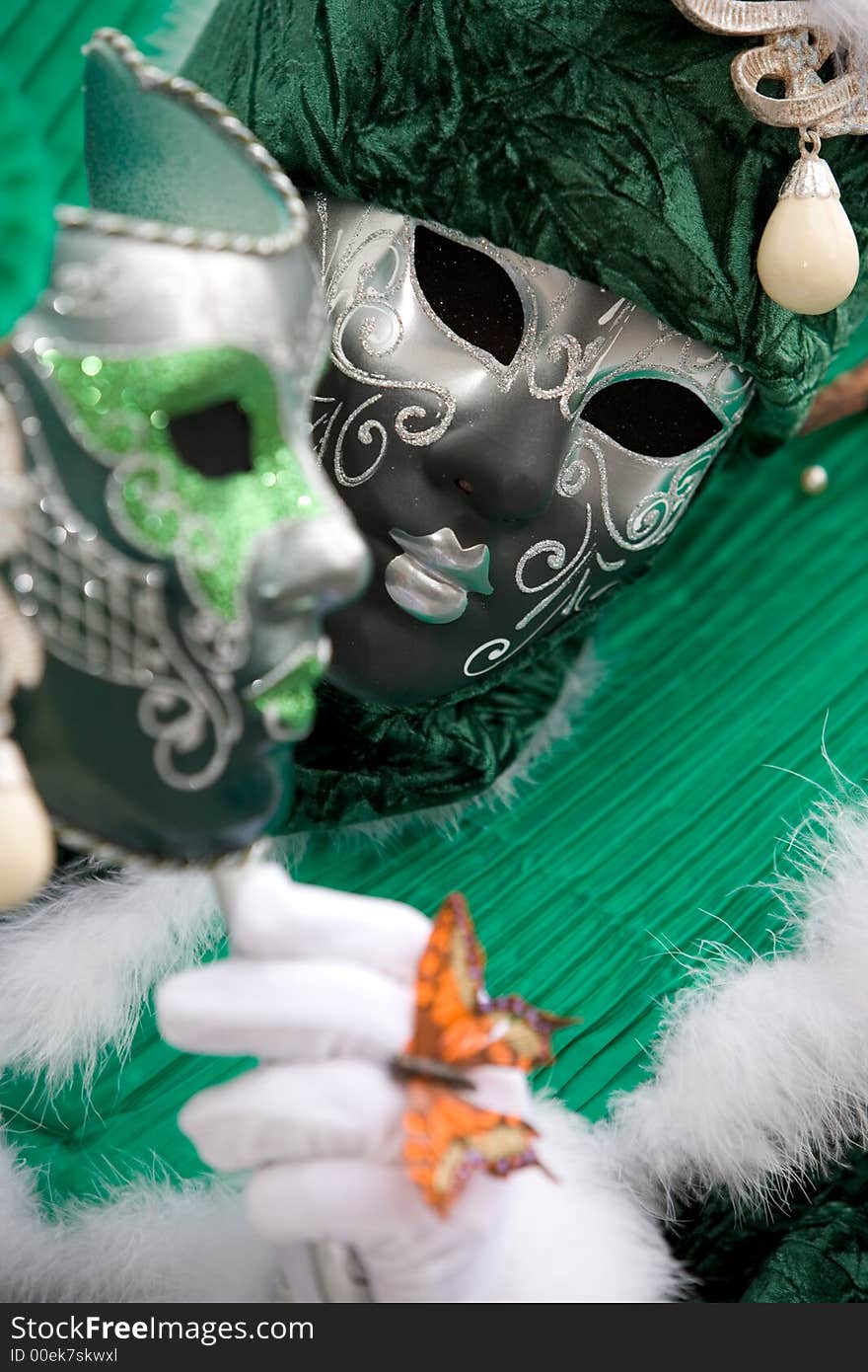 A venetian man in a grey mask and green costume holding a green mask. A venetian man in a grey mask and green costume holding a green mask