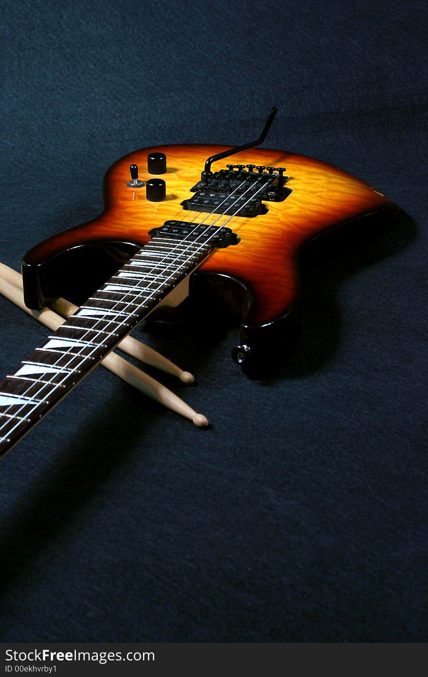 Close up view of electric guitar and drumstick on a black background