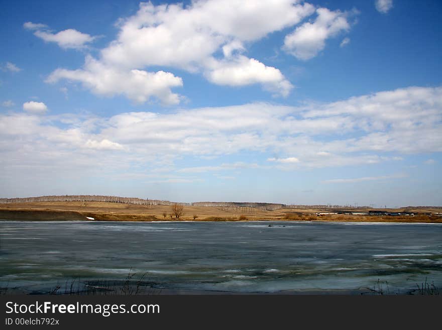 Spring landscape with lake the covered thawing ice and village on a background. Spring landscape with lake the covered thawing ice and village on a background.