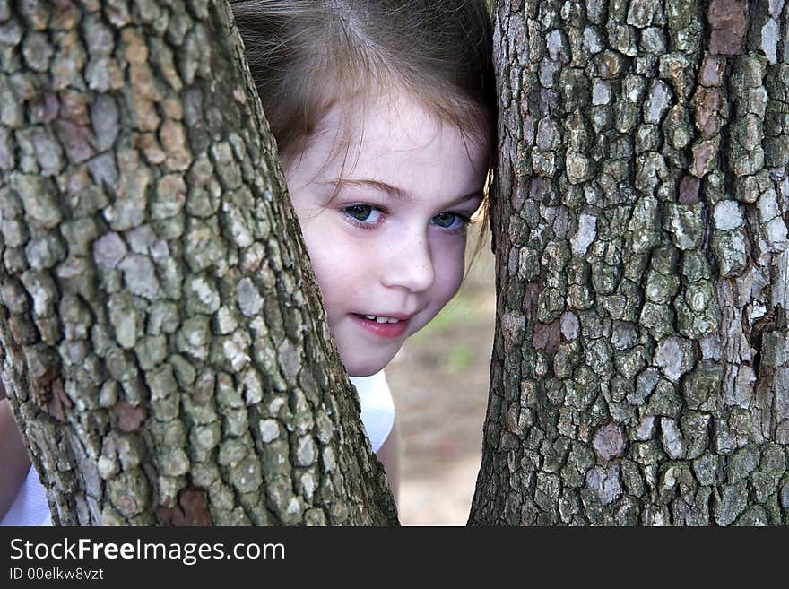 Little Girl Peeking Through the Tree Trunks in a Park. Little Girl Peeking Through the Tree Trunks in a Park