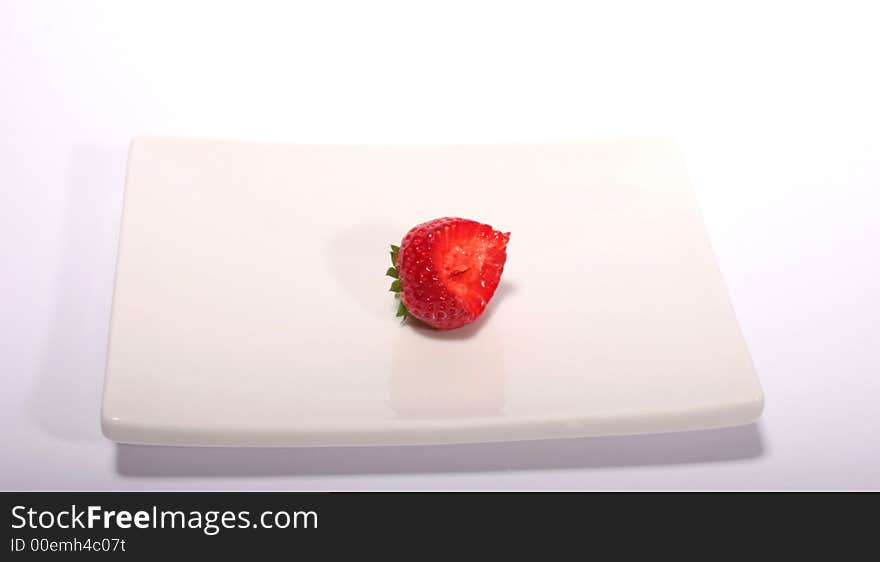 A half-bitten strawberry on a white plate against a white background