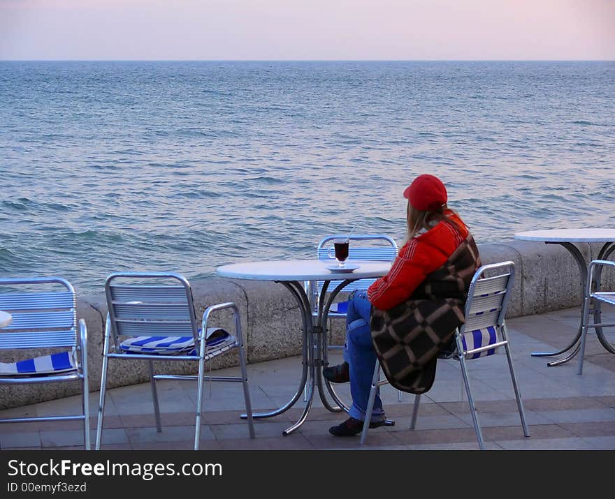 The girl sitting on quay of Black sea with a glass mulled wine