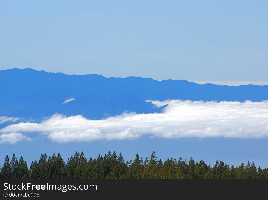 Taken with telephoto lens, the island of La Gomera is seen with floating,stratified clouds, over the Atlantic ocean and a forest on Tenerife. Taken with telephoto lens, the island of La Gomera is seen with floating,stratified clouds, over the Atlantic ocean and a forest on Tenerife