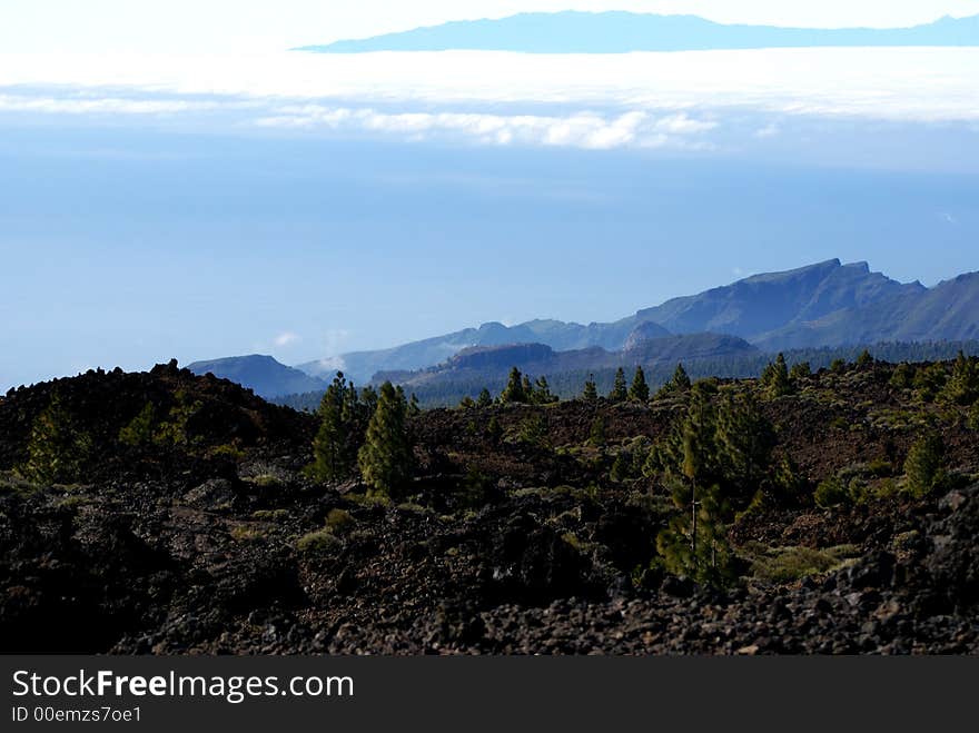 Looking through volcanic rock on top of Mt. Teide giving a perspective of La Gomera being above the floating clouds above the Atlantic. The elevation on the volcano provides a different perspective on the other Canary Islands. Looking through volcanic rock on top of Mt. Teide giving a perspective of La Gomera being above the floating clouds above the Atlantic. The elevation on the volcano provides a different perspective on the other Canary Islands.