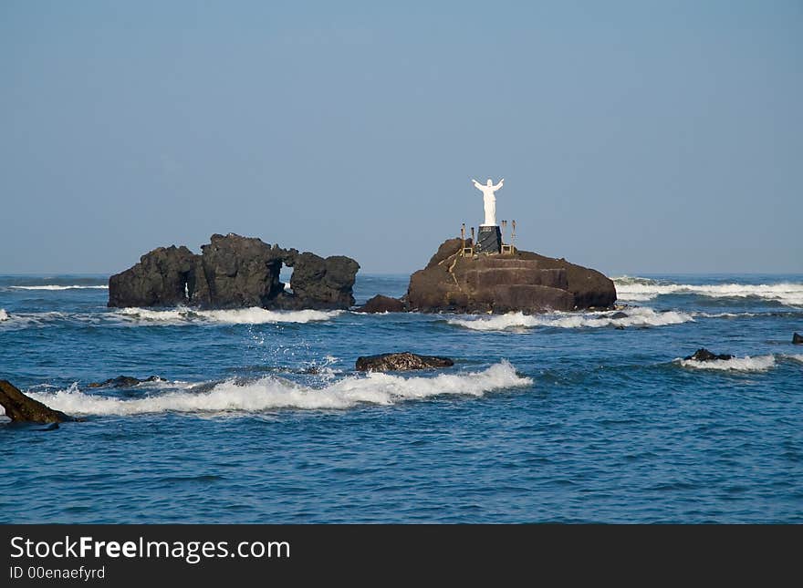 A statue of Jesus stands on a small island of volcanic rocks. A statue of Jesus stands on a small island of volcanic rocks