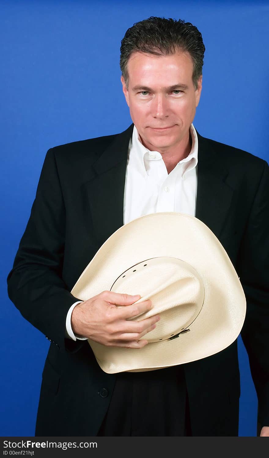 Mature, handsome, white male wearing a black suite and a white shirt holding a cowboy hat with one hand. Mature, handsome, white male wearing a black suite and a white shirt holding a cowboy hat with one hand.