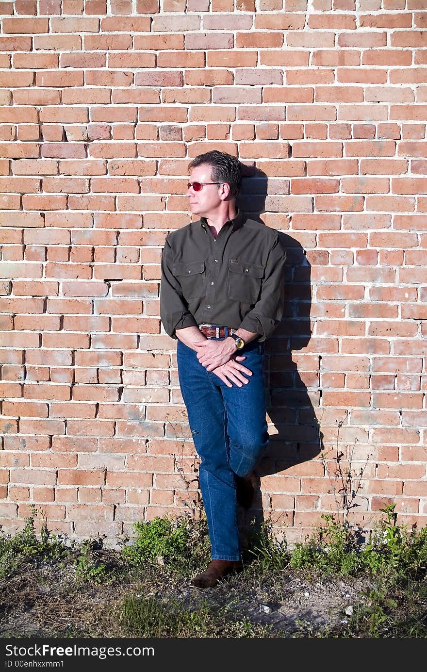 Handsome white male in sunglasses leaning against an old brick wall in the late afternoon as if waiting for someone or something. Handsome white male in sunglasses leaning against an old brick wall in the late afternoon as if waiting for someone or something