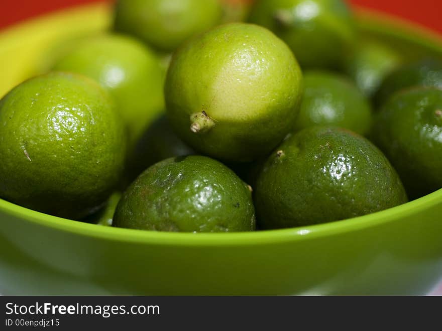 Limes up close in a green bowel against red background.