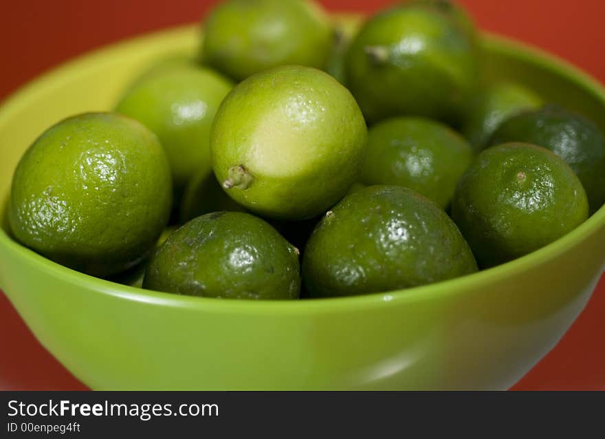 Limes up close in a green bowel against red background.