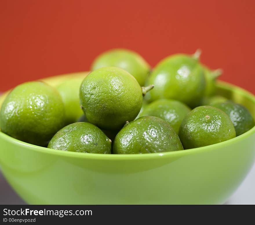 Limes up close in a green bowel against red background.